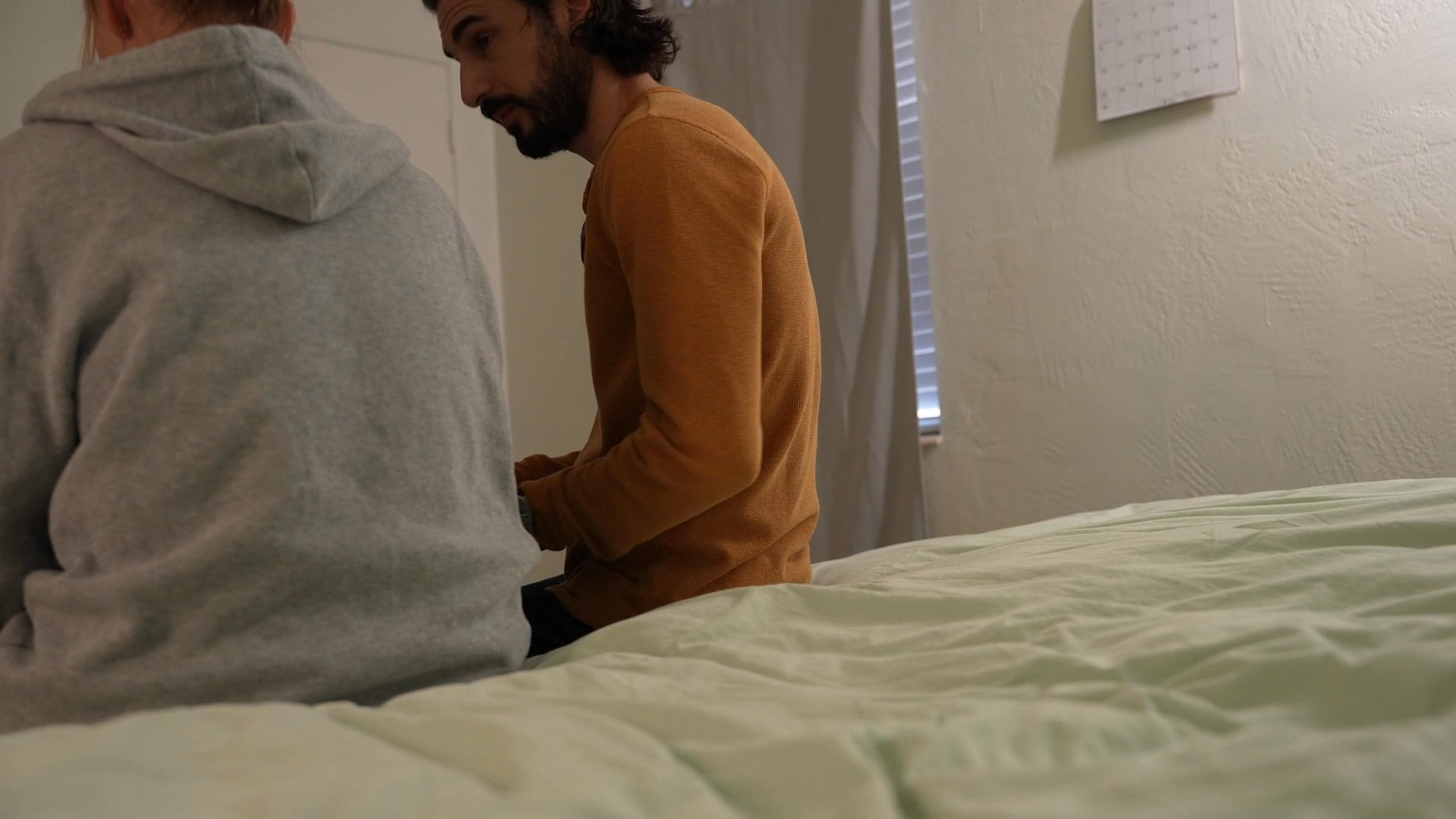 A man offers comfort and emotional support to a woman sitting on the edge of a bed. Their interaction conveys a shared moment of vulnerability and quiet empathy.