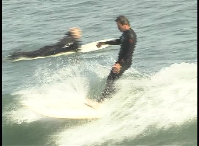 A surfer wearing a black wetsuit skillfully balances on a surfboard while traversing a breaking ocean wave.