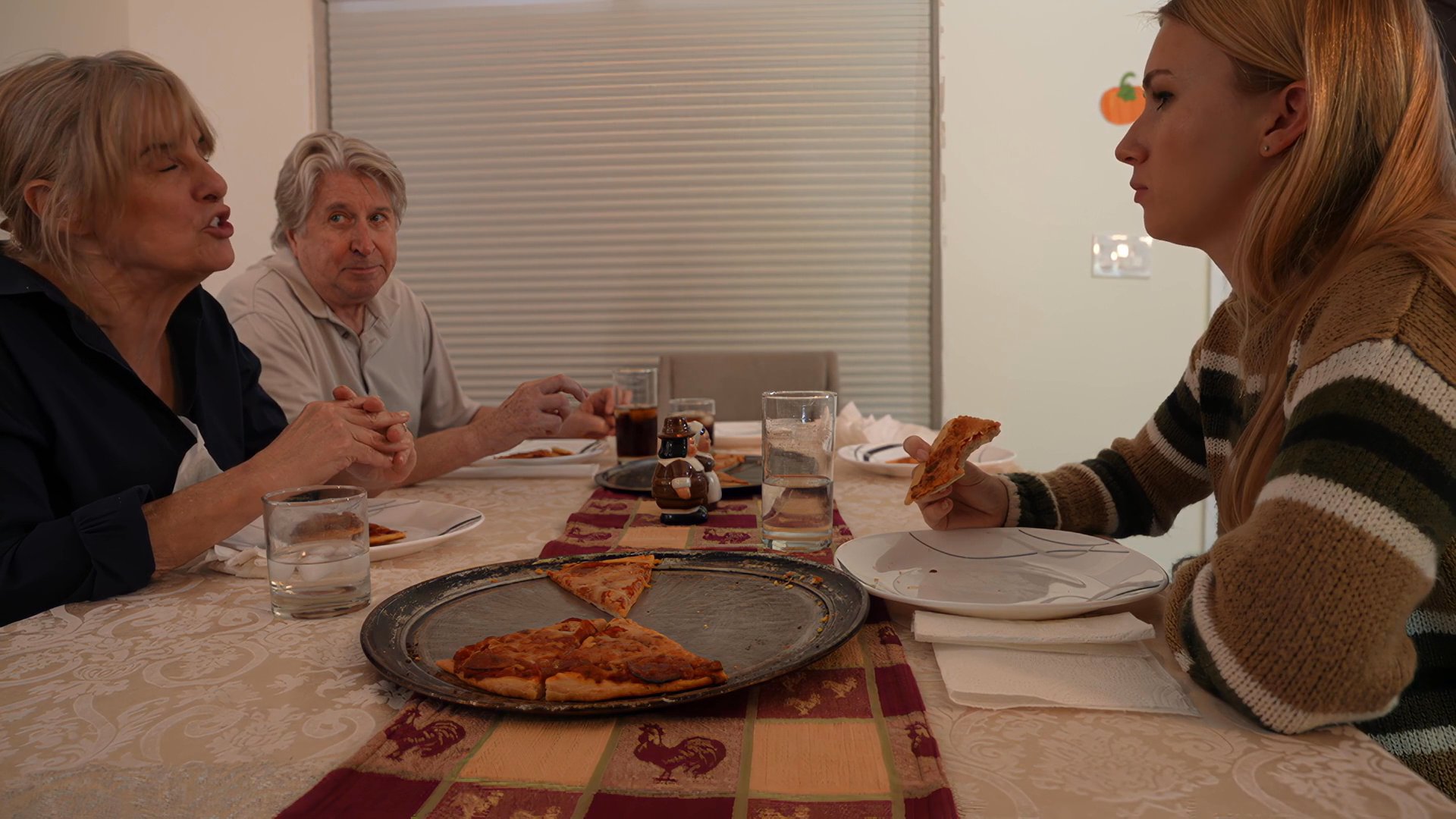 Three individuals engage in conversation while seated around a dining table at home, enjoying a meal together. The atmosphere is casual and reflects a typical domestic social setting.