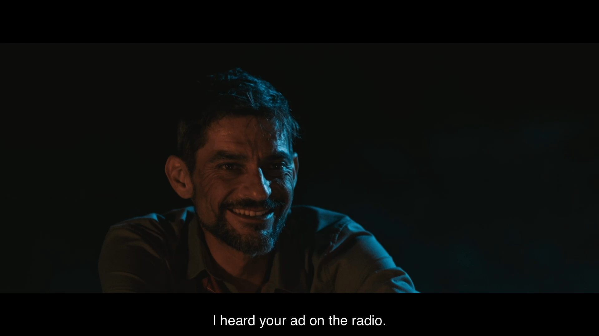Two men sit together in the dark by a fire, discussing an advertising slogan heard on the radio and sharing personal reflections. The conversation shifts from casual professional talk to a somber admission about a separation from family.