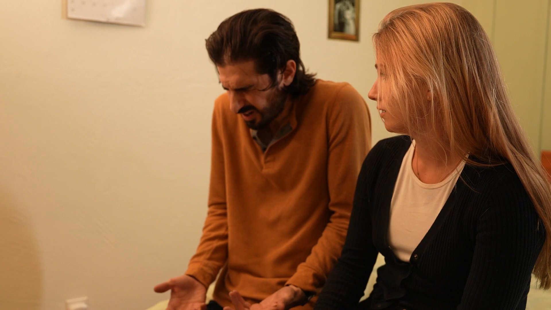 A man and woman engage in a focused, serious discussion while sitting together in a private setting. They maintain consistent eye contact and exhibit body language indicative of an intense or deeply personal conversation.