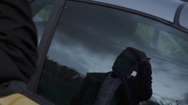 Man adjusting hair in reflection of a car