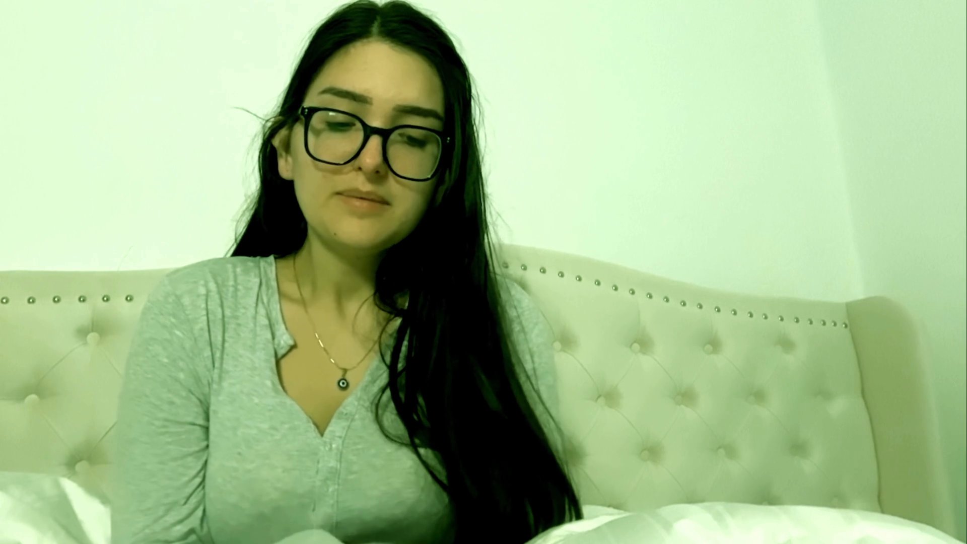A woman sits in a bedroom and speaks directly to the camera, sharing commentary and engaging in a discussion.