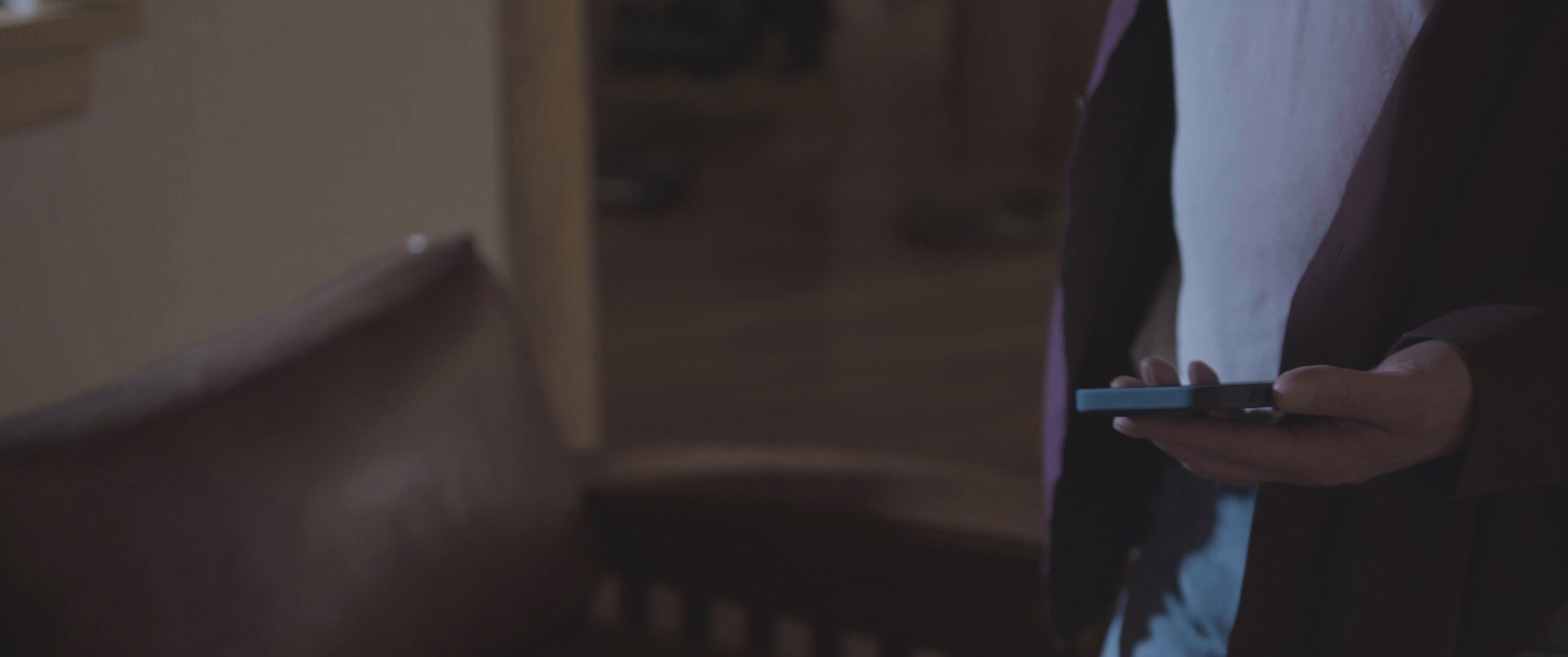 A man engages in a tense phone conversation while moving through a living room space, passing a phone to a woman resting on a sofa.