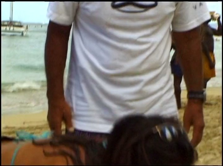 An instructor guides a student through proper surfing techniques on the sand before they practice in the ocean waves. The session emphasizes balancing and physical form required for riding the water.