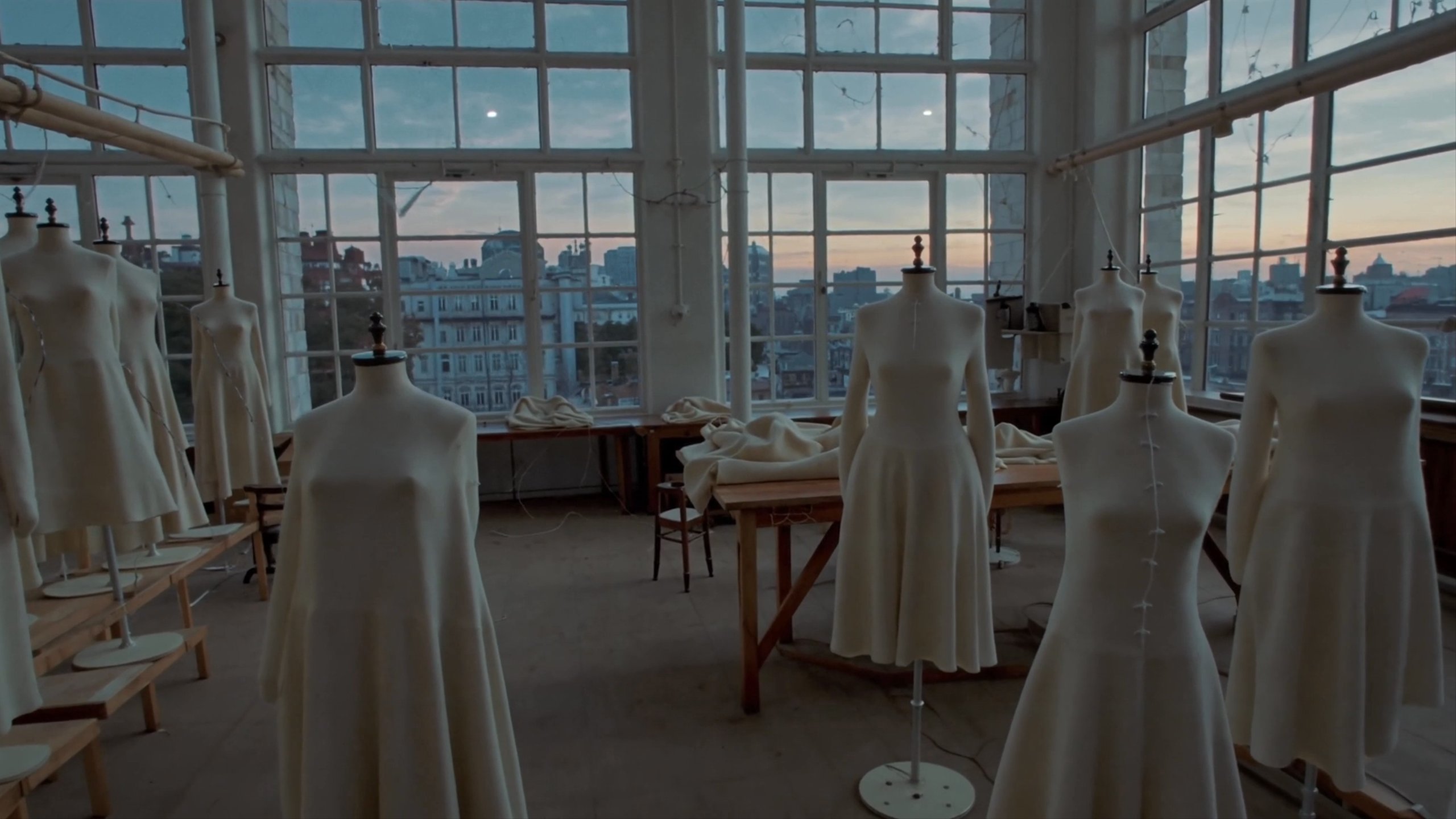 A slow push-in across a couture atelier at dawn, rows of dress forms draped in unbleached muslin.