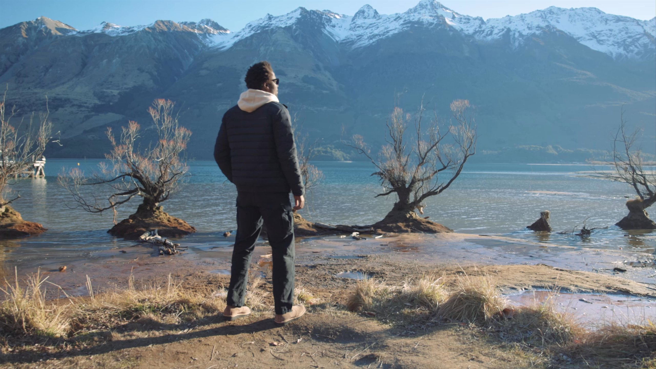 Video of man turning along river shore with snow capped mountains in New Zealand