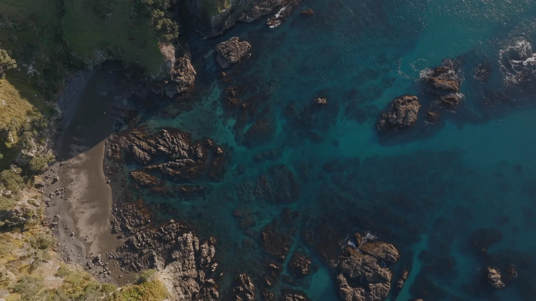 Aerial top-down of turquoise shallows and volcanic rock at a Mataka Station beach