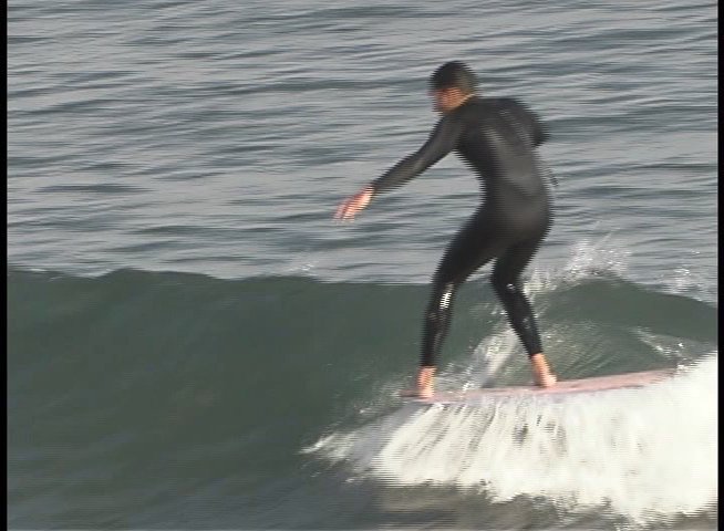 Athletes in wetsuits navigate waves on surfboards in a coastal environment. The sequence highlights their balance and technique while maneuvering through the rolling surf.