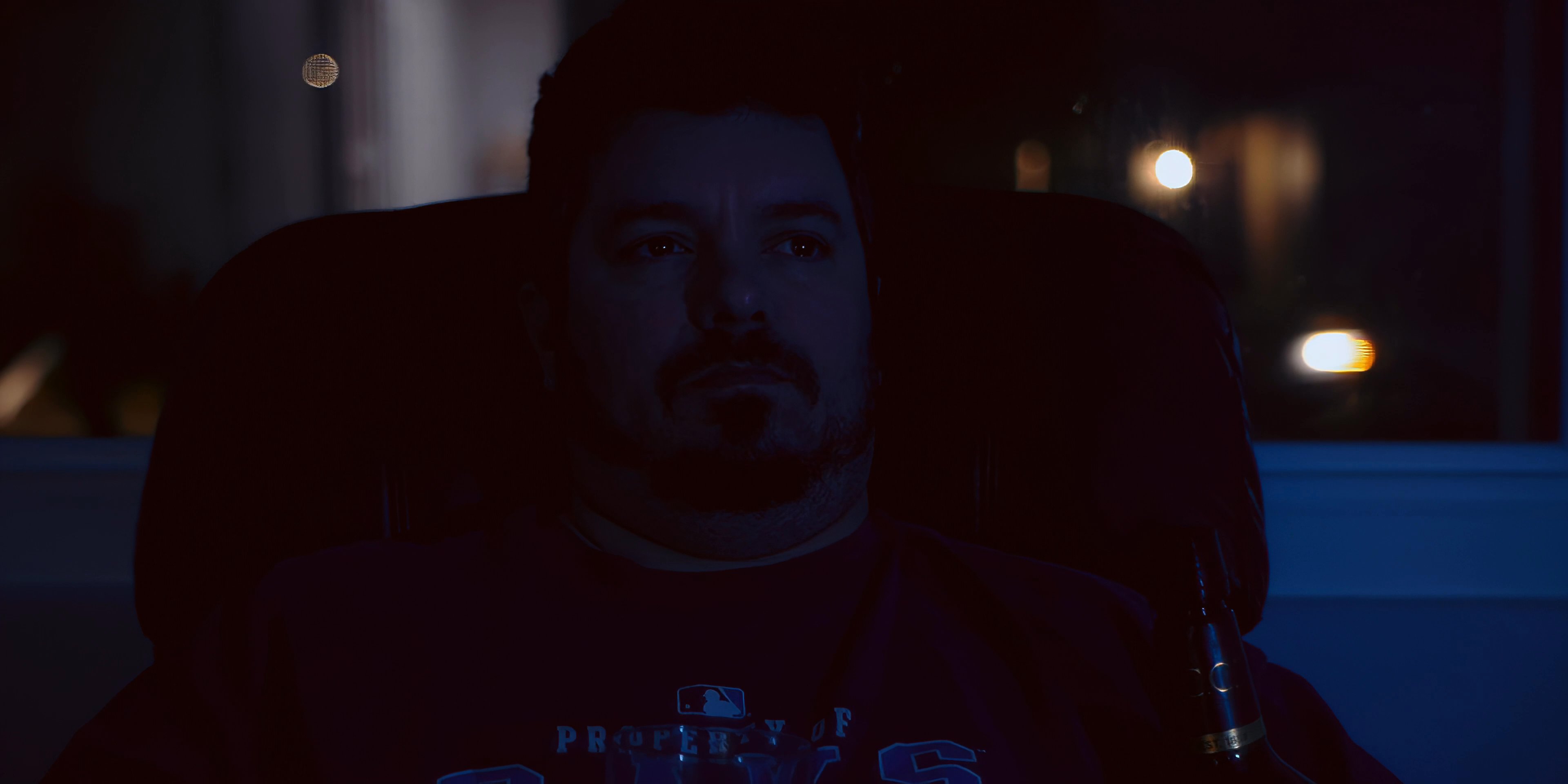 A man sits alone in a dimly lit room at night, drinking from a glass while relaxing in his home environment.
