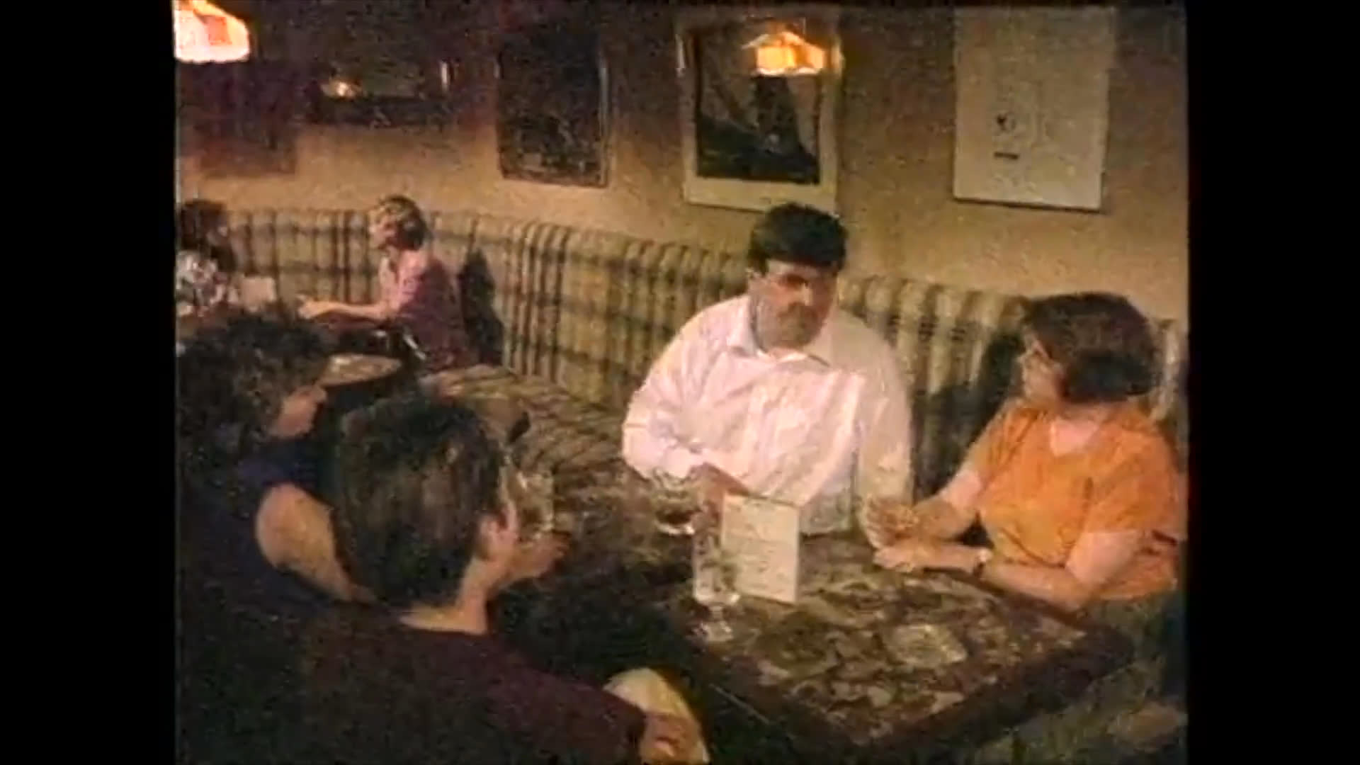 Two individuals engage in a dramatic conversation, transitioning to a scene inside a restaurant where patrons view a televised segment featuring a man speaking directly to the camera.