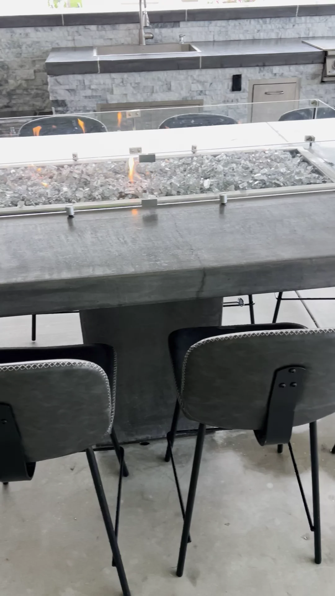 Built-in fire pit bar with smooth concrete top, fire glass & glass wind guard