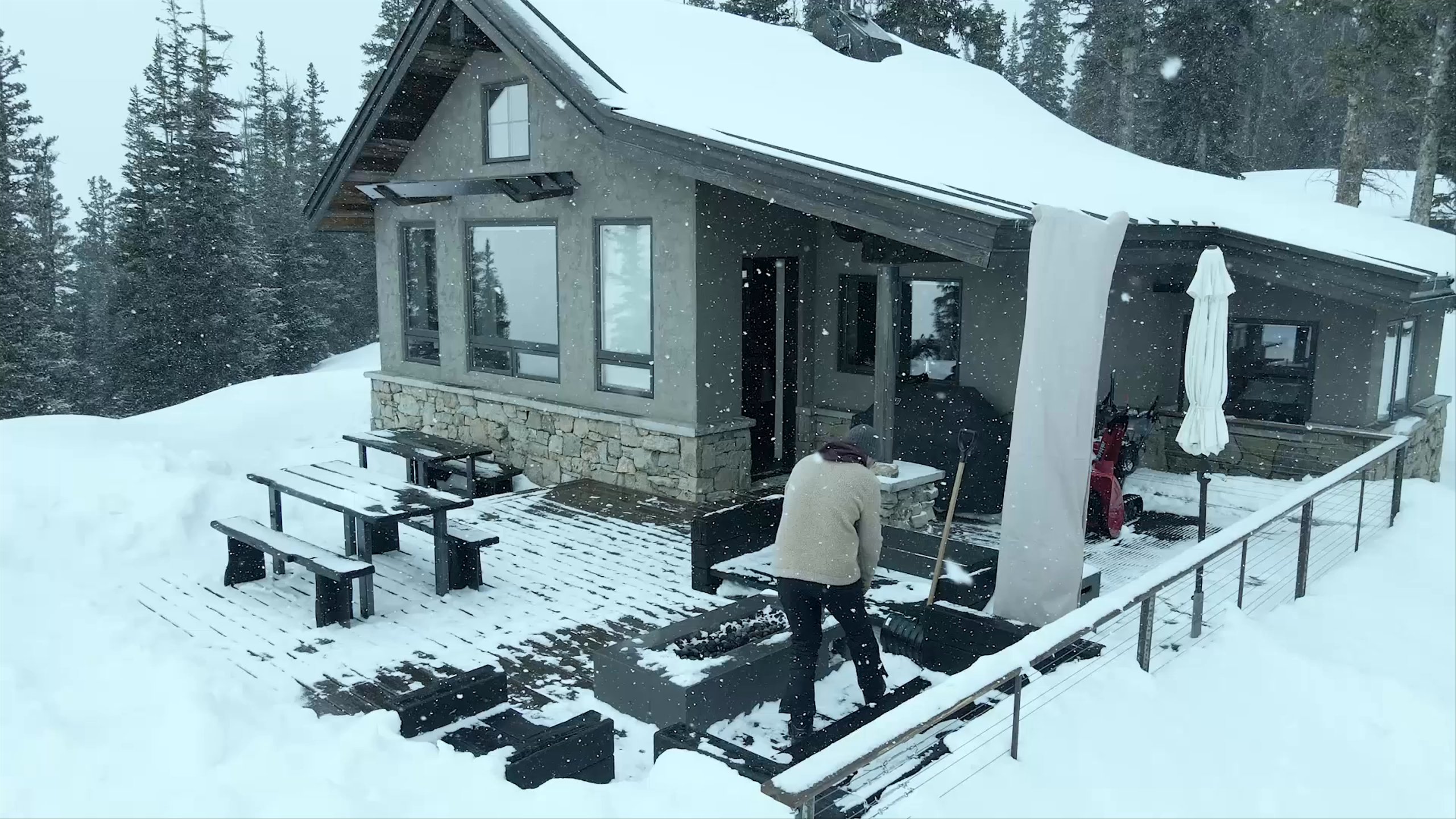 Video drone of man outside cabin pulling back to reveal full snowy mountain