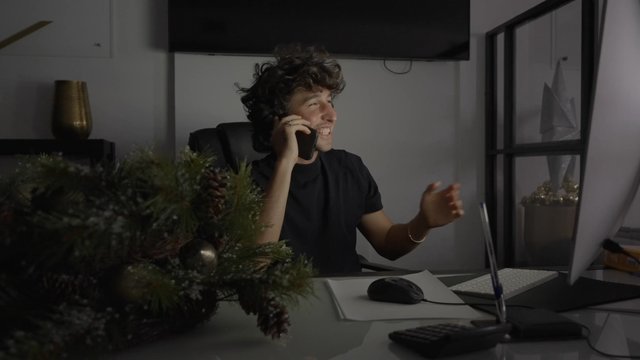 A man laughing while sitting at his desk and talking on his phone