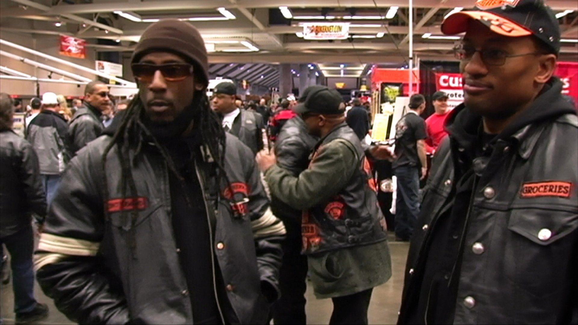 Two individuals participate in an interview at a bustling motorcycle exhibition filled with custom bikes and industry attendees.