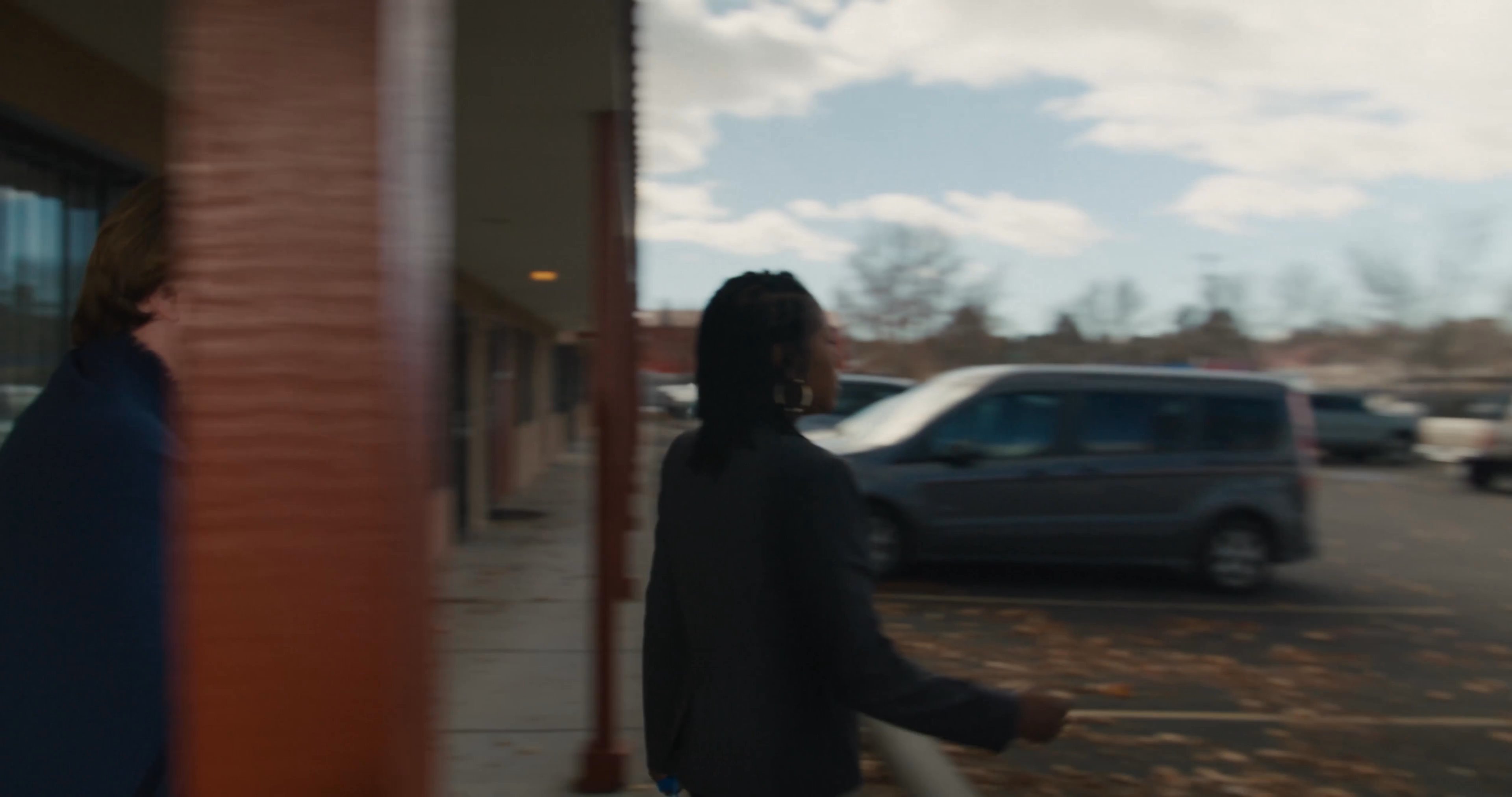 A man and a woman in business attire interact with a man at a motel room door before exiting across the parking lot with bags. The sequence depicts a tense professional or formal exchange ending in the departure of the motel guests.