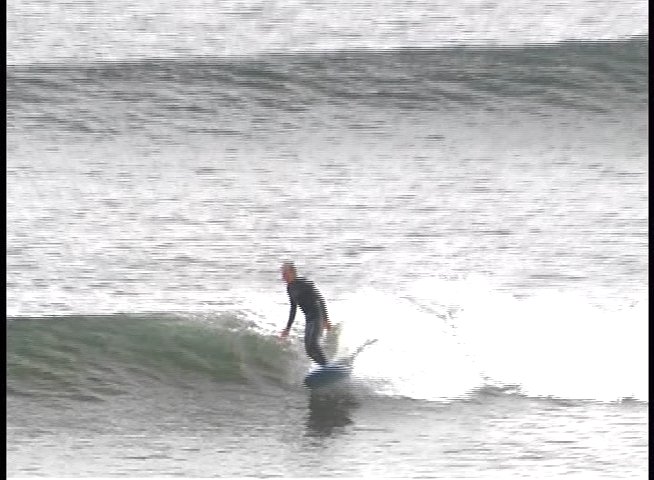 A surfer in a wetsuit maneuvers across an open wave, maintaining balance and posture while carving through the water.