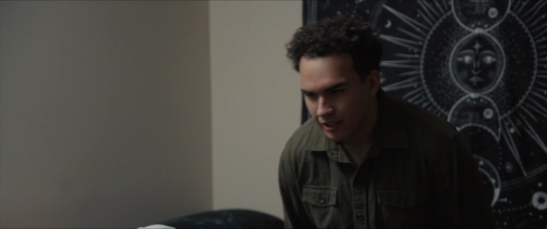 Two individuals engage in a brief, casual conversation within an indoor environment. One person subsequently settles at a desk to eat while another passes by in the background.