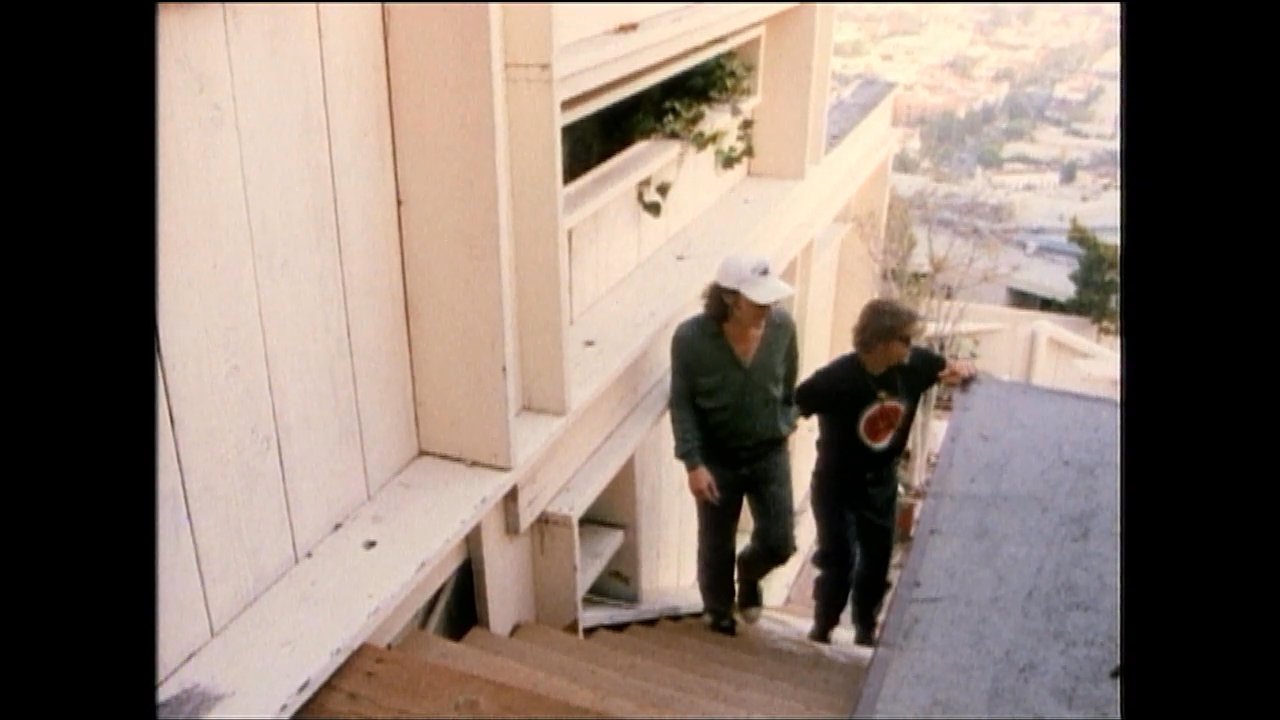 A production crew and actors review scripts and coordinate staging on an outdoor residential staircase set. The individuals discuss performance details before transitioning into the filming process.