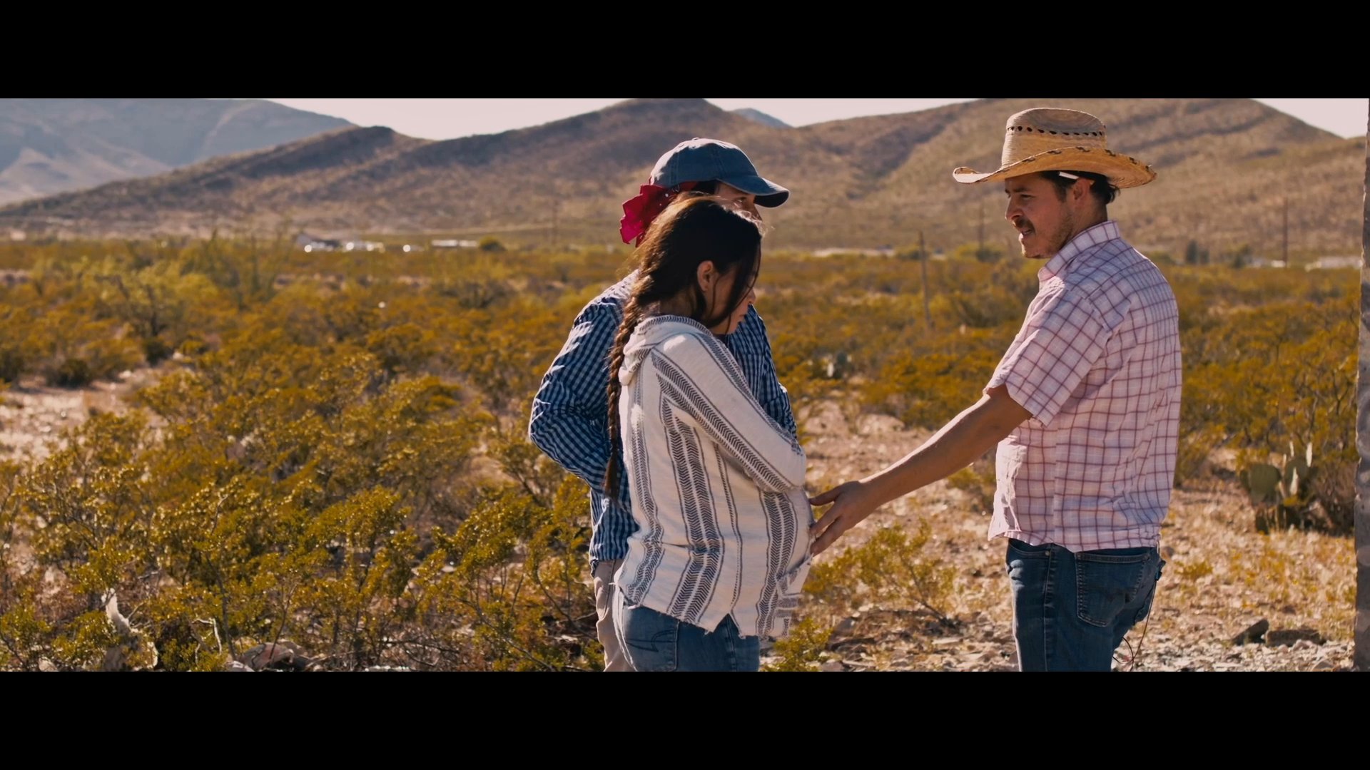 Three individuals engage in a tense, pointed conversation within an expansive, sun-drenched desert environment. The exchange focuses on a delicate interpersonal matter, concluding with an uneasy resolution.