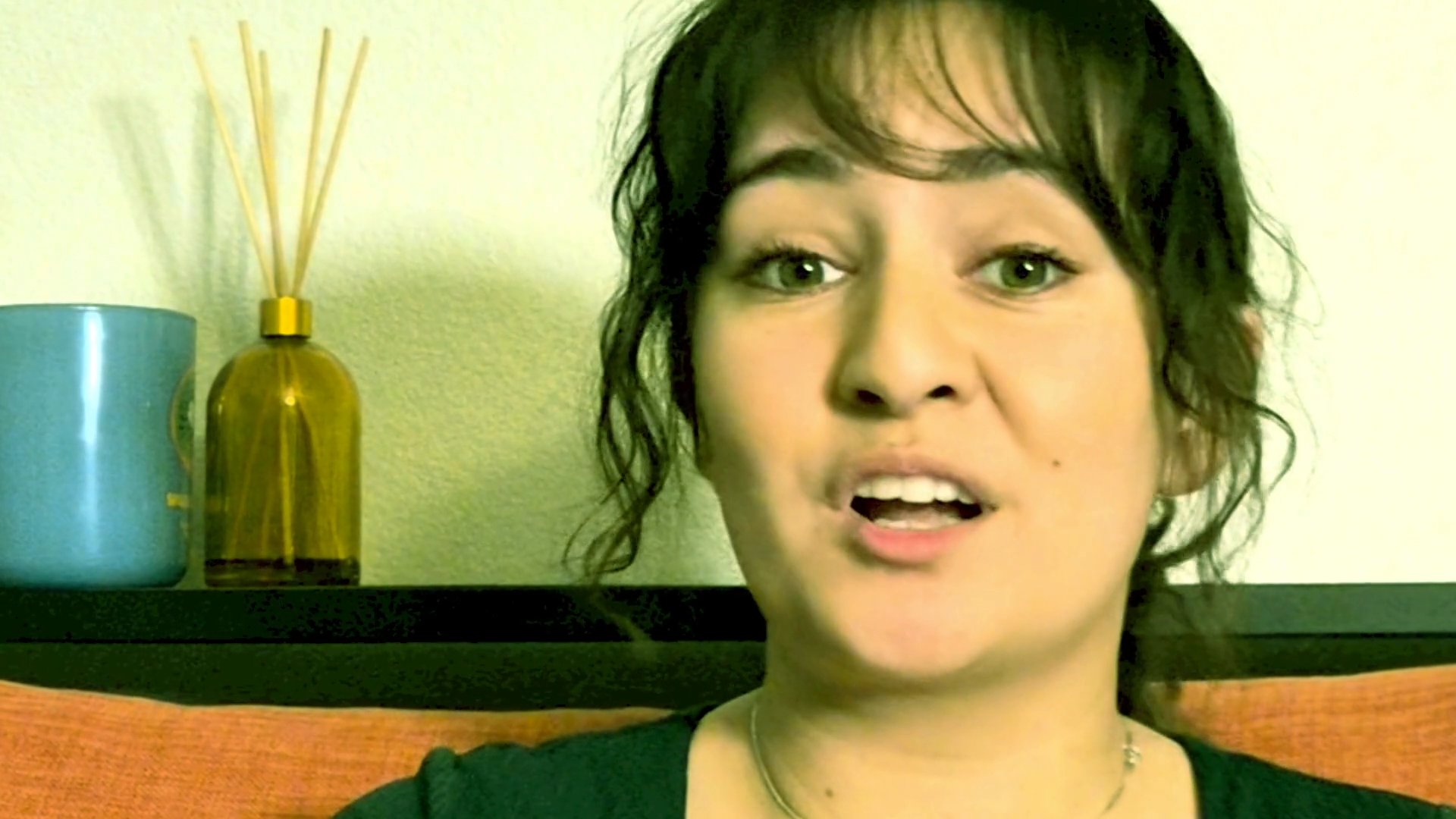 A woman engages in a casual, expressive conversation while seated, using hand gestures to emphasize her points. The setting is a quiet, comfortable indoor space.