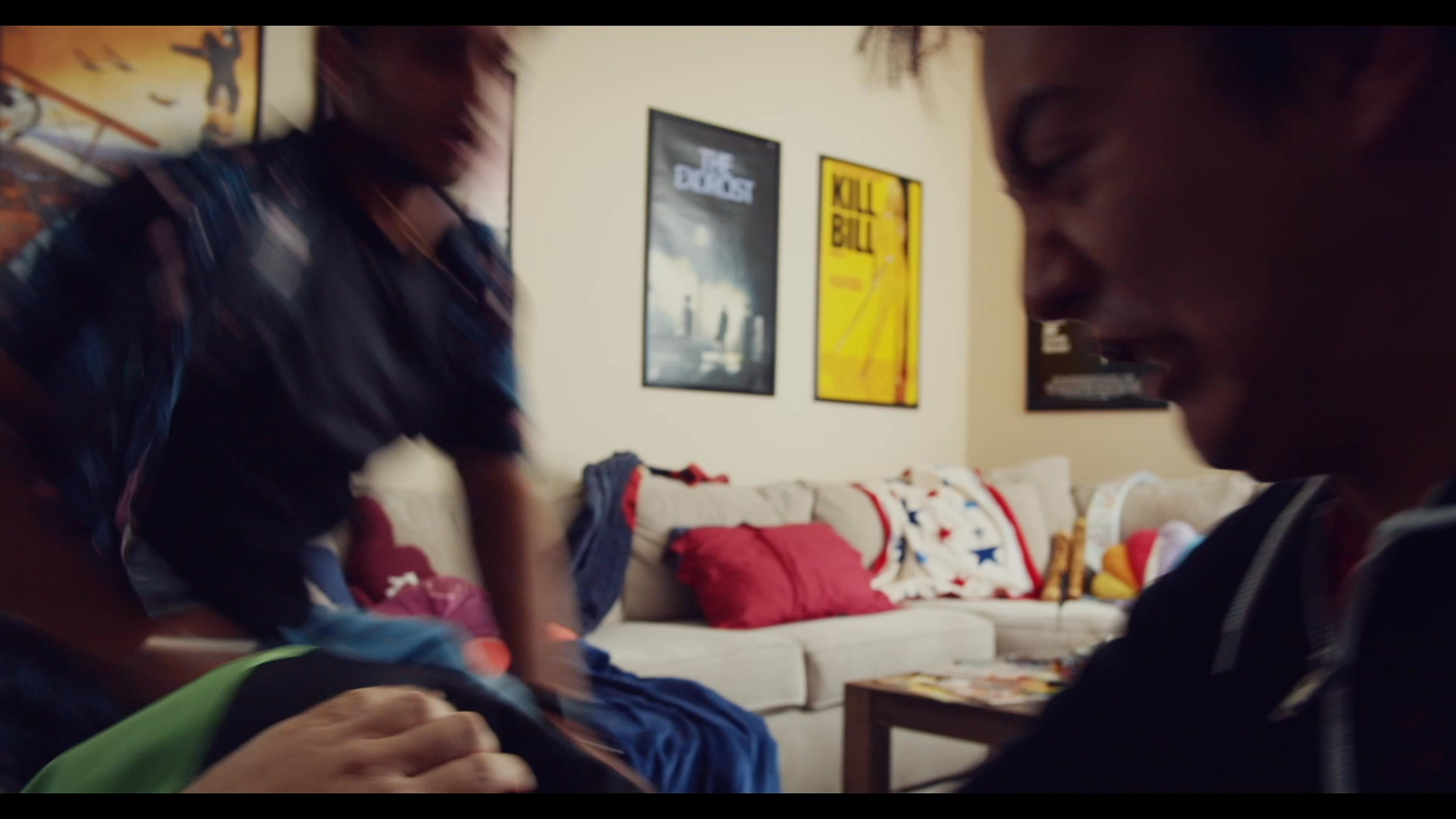 Two individuals engage in a violent physical altercation within a living room, wrestling and grappling near furniture and musical equipment.