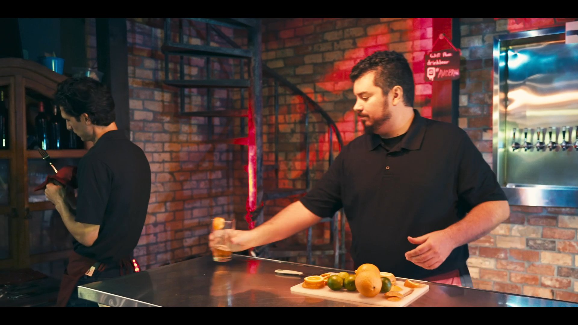 A waitstaff member interacts with patrons at a table in a pub-style restaurant, while staff at the bar discuss menu items and service details.