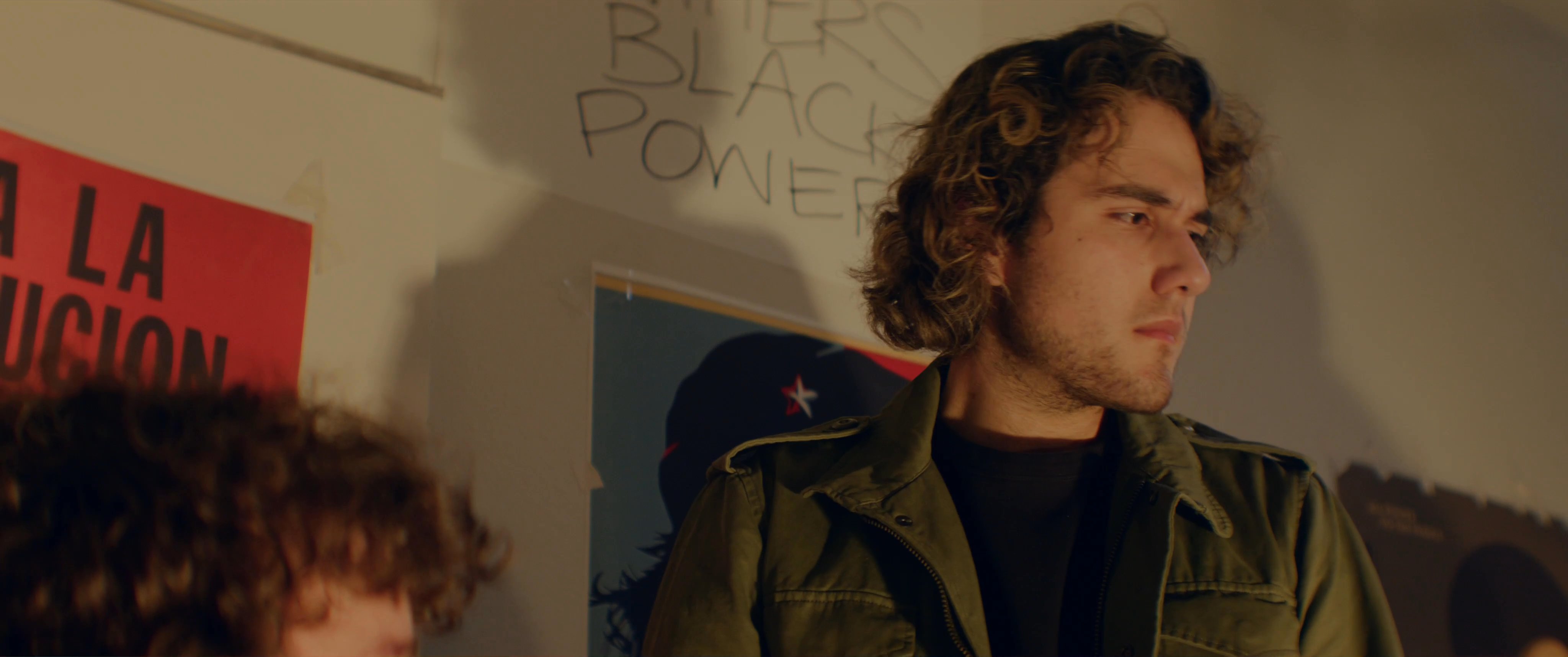 A diverse group of activists gathers in a dimly lit, poster-adorned space to engage in a heated, intense discussion about their movement's objectives. They exchange passionate viewpoints and critique current strategies while documenting their proceedings.