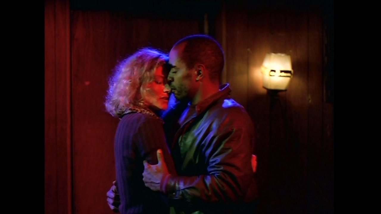 A man and woman share an intimate, close embrace within a softly lit, warm-toned environment. The scene captures a quiet moment of emotional connection and closeness between the two individuals.