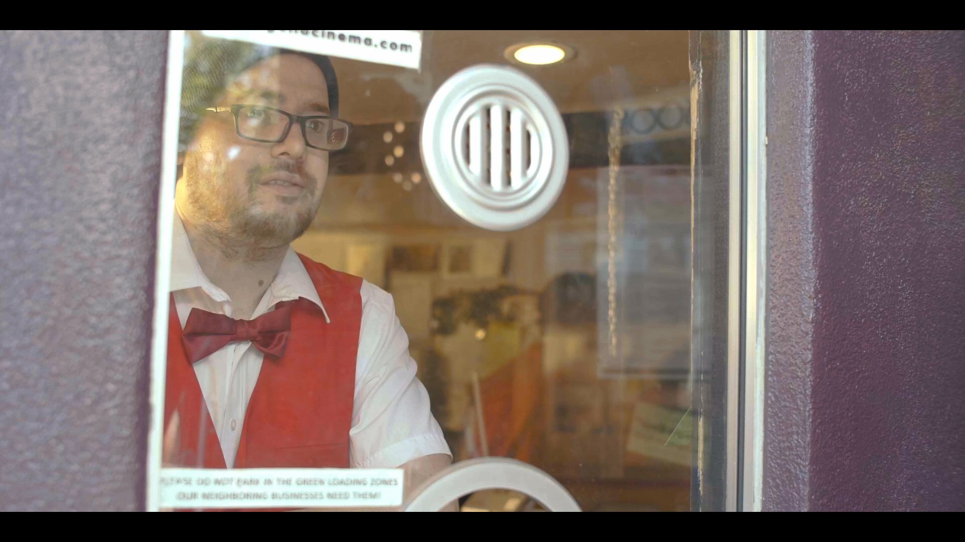 A man speaks to a service clerk through a glass window at a ticketing booth while other patrons wait in line.