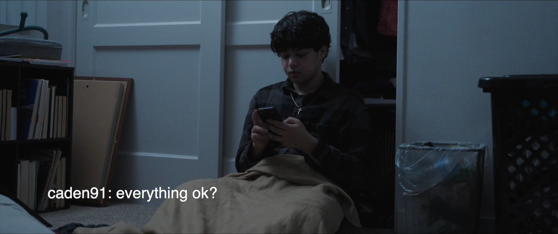 An individual sits alone in a bedroom, engaged in a text message exchange on a smartphone. The scene highlights the quiet, reflective nature of digital interaction.