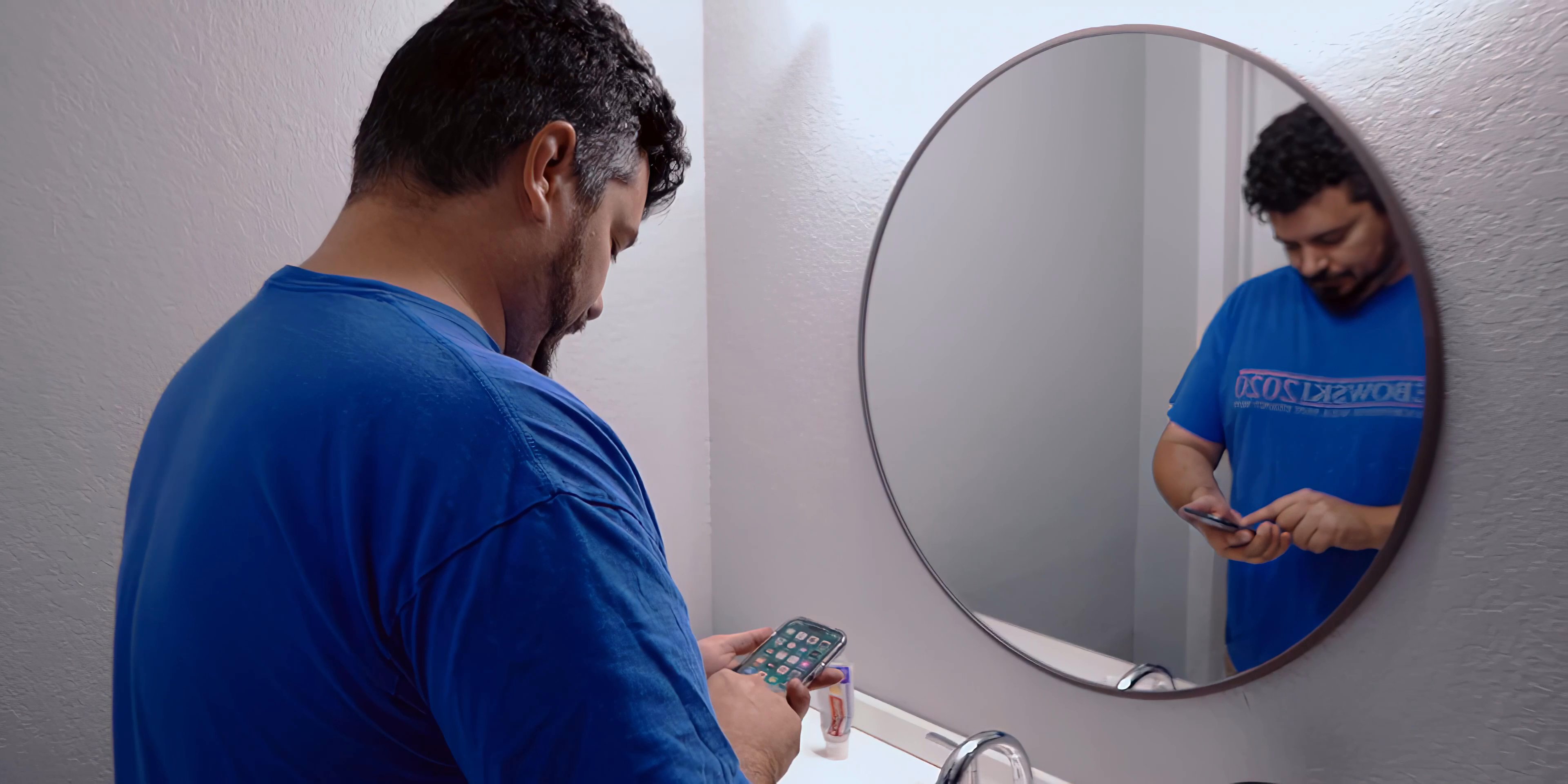 The sequence opens with opening production credits displayed over a bedroom, followed by a transition to a man standing at a bathroom vanity checking his smartphone.