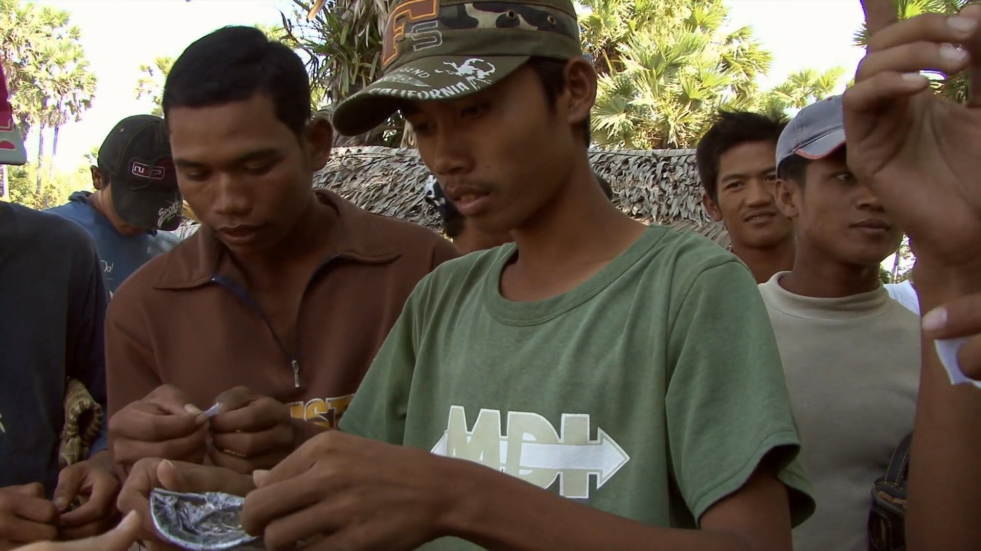 A group of men gather outdoors to receive and try on new pairs of sunglasses. The participants examine the eyewear, place them on their faces, and display them to the group.