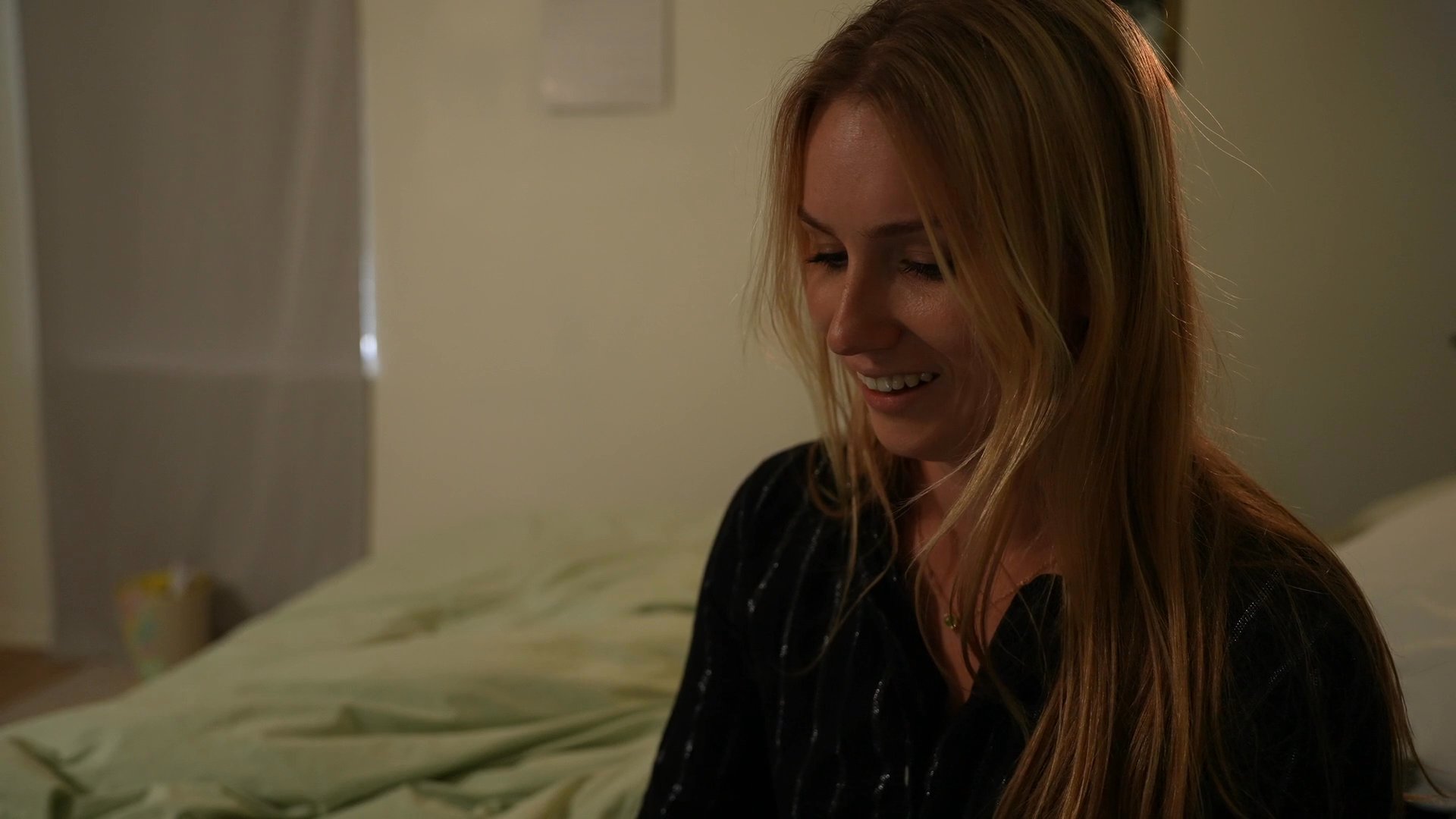 A man and a woman engage in a warm, lighthearted conversation within a bedroom environment, culminating in the woman enjoying a beverage. The interaction demonstrates a sense of personal connection and relaxed social engagement.