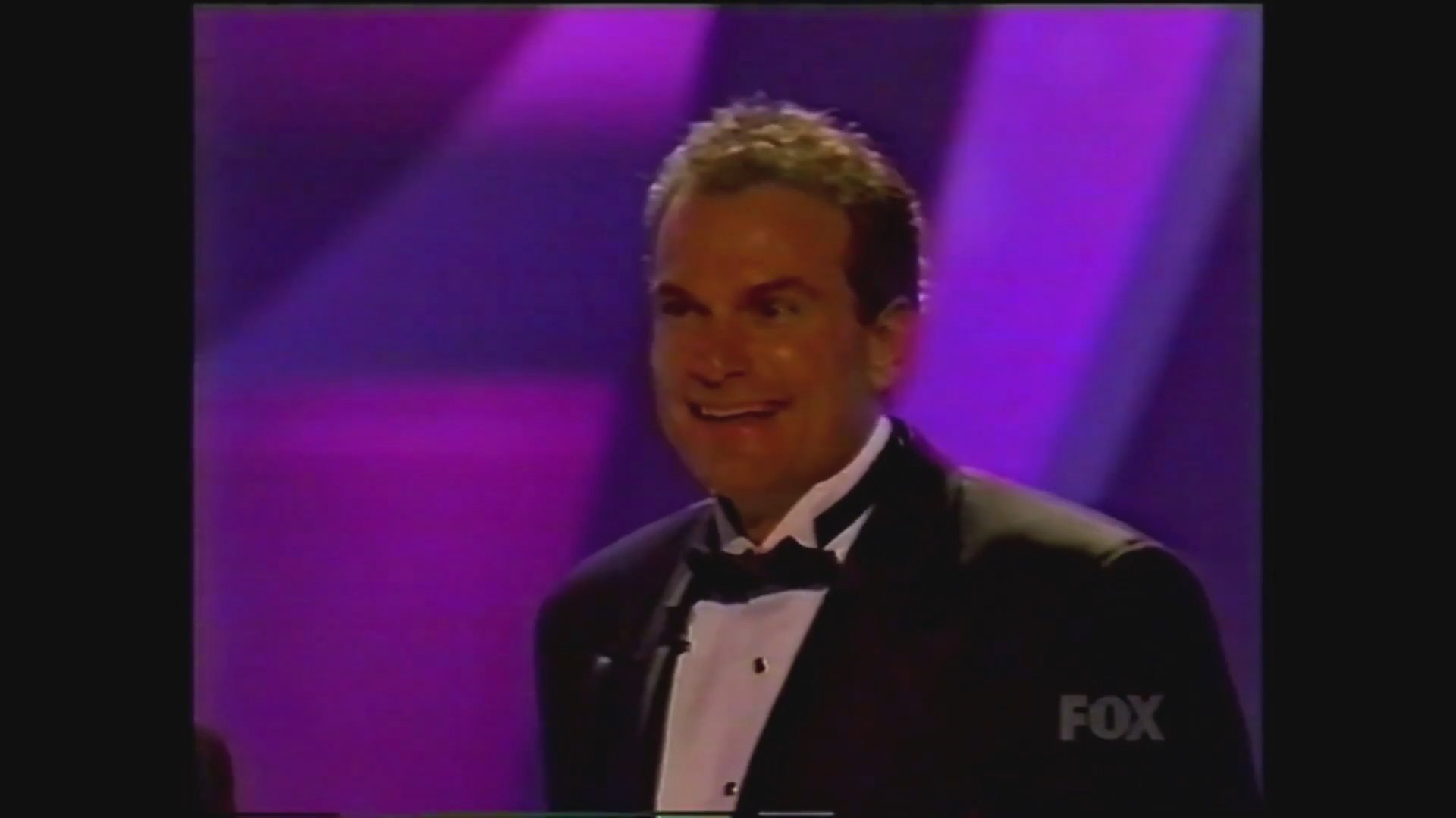 A television dating show concludes with a staged wedding ceremony involving contestants on a brightly lit studio stage. The participants dressed in formal bridal attire interact and exchange a celebratory kiss as the program segment wraps.