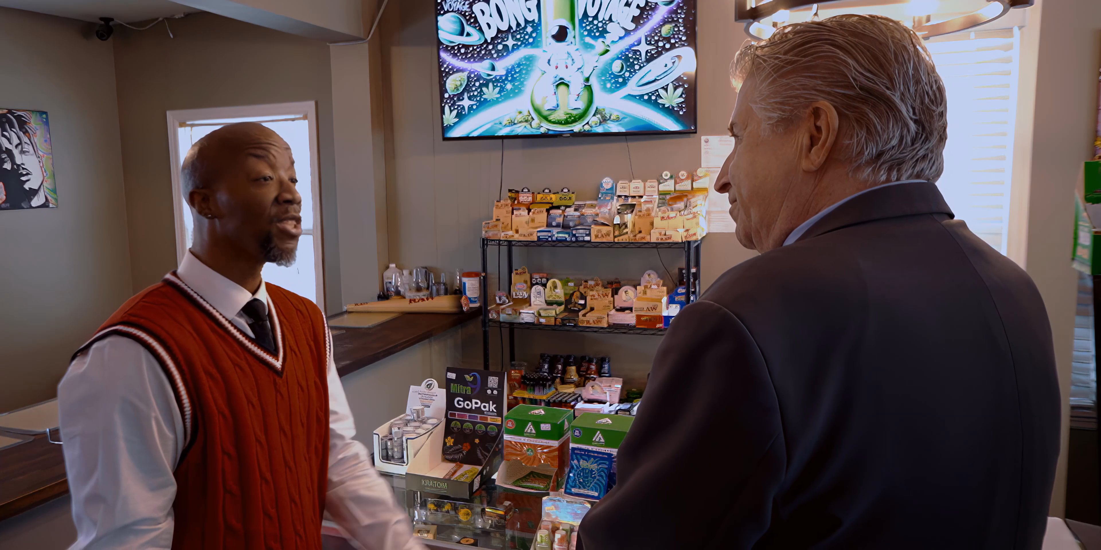 Two individuals engage in a professional discussion inside a retail storefront. A third person subsequently joins the conversation, facilitating a transition in the interaction.