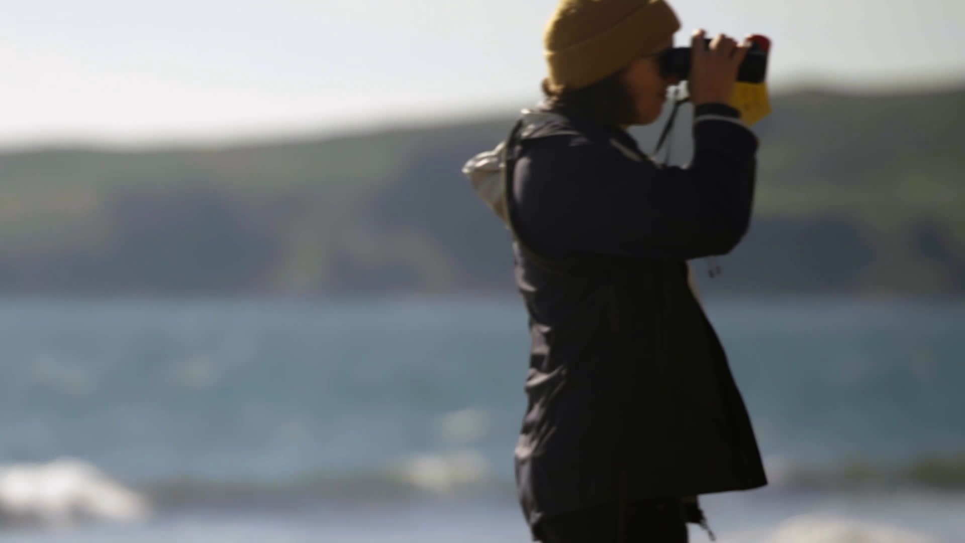 Dr. Allen mentors field assistant Marjorie as they walk along a sunlit shoreline and survey seals. Marjorie scans the coast with binoculars while they coordinate their fieldwork.