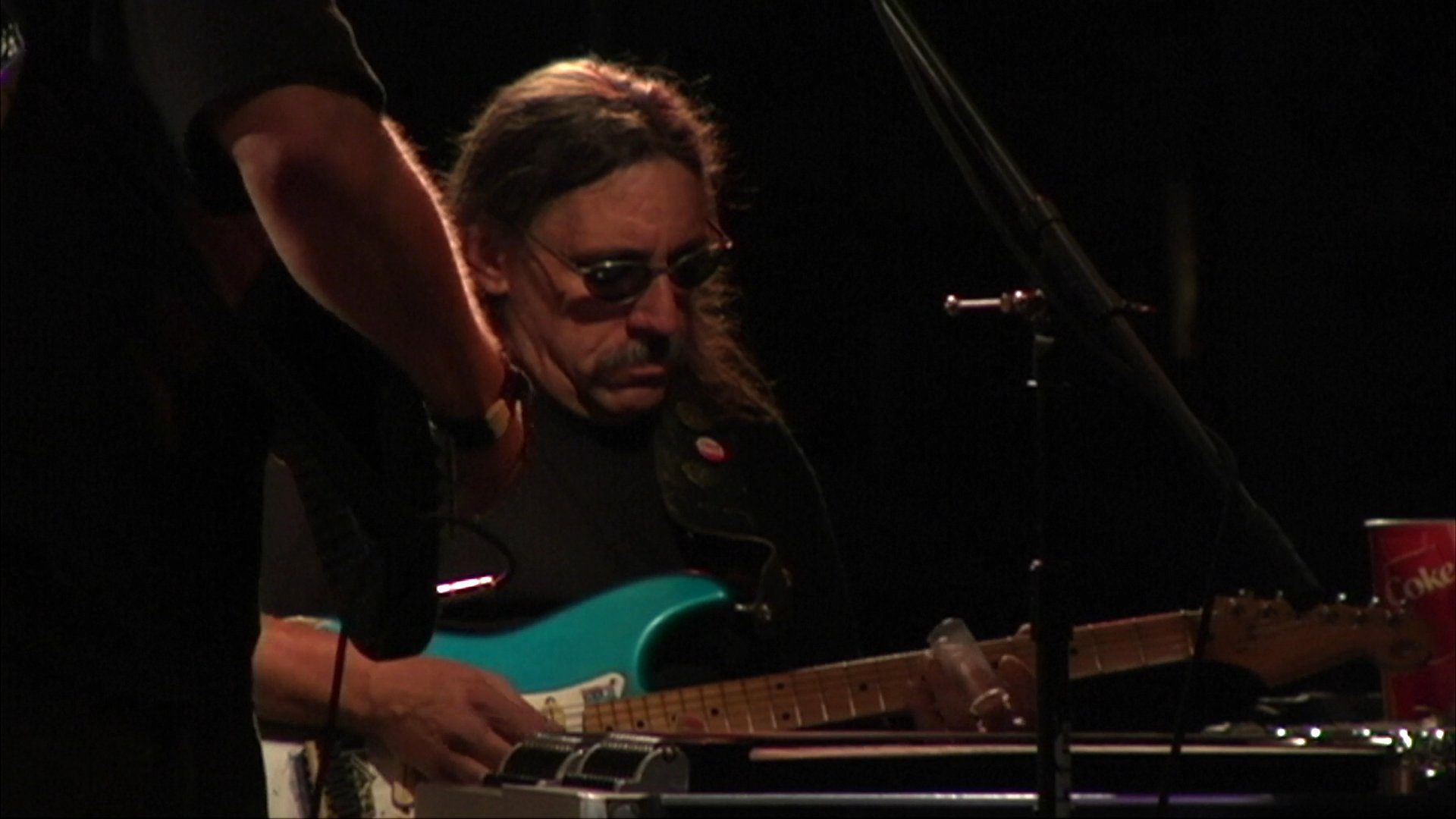 A live band performs for a crowd on a dimly lit bar stage while patrons dance and enjoy the music. The sequence captures musicians playing electric guitars and singing, interspersed with shots of the energetic audience.