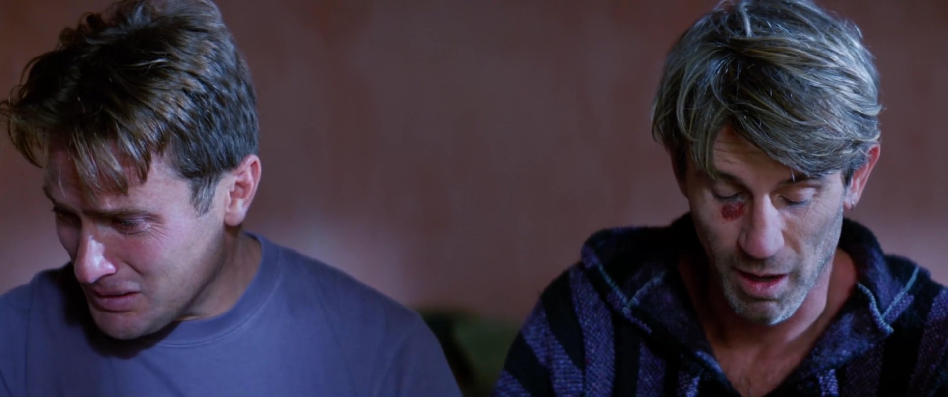 Two men engage in an intense, emotionally charged conversation within an indoor setting, with one individual appearing visibly distressed and tearful.