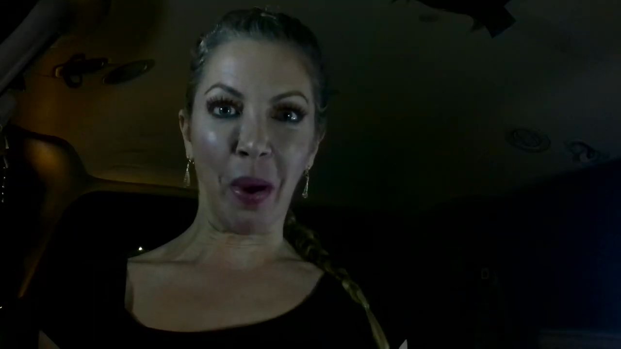 A woman sits inside a parked van at night and speaks directly to the camera with expressive gestures.