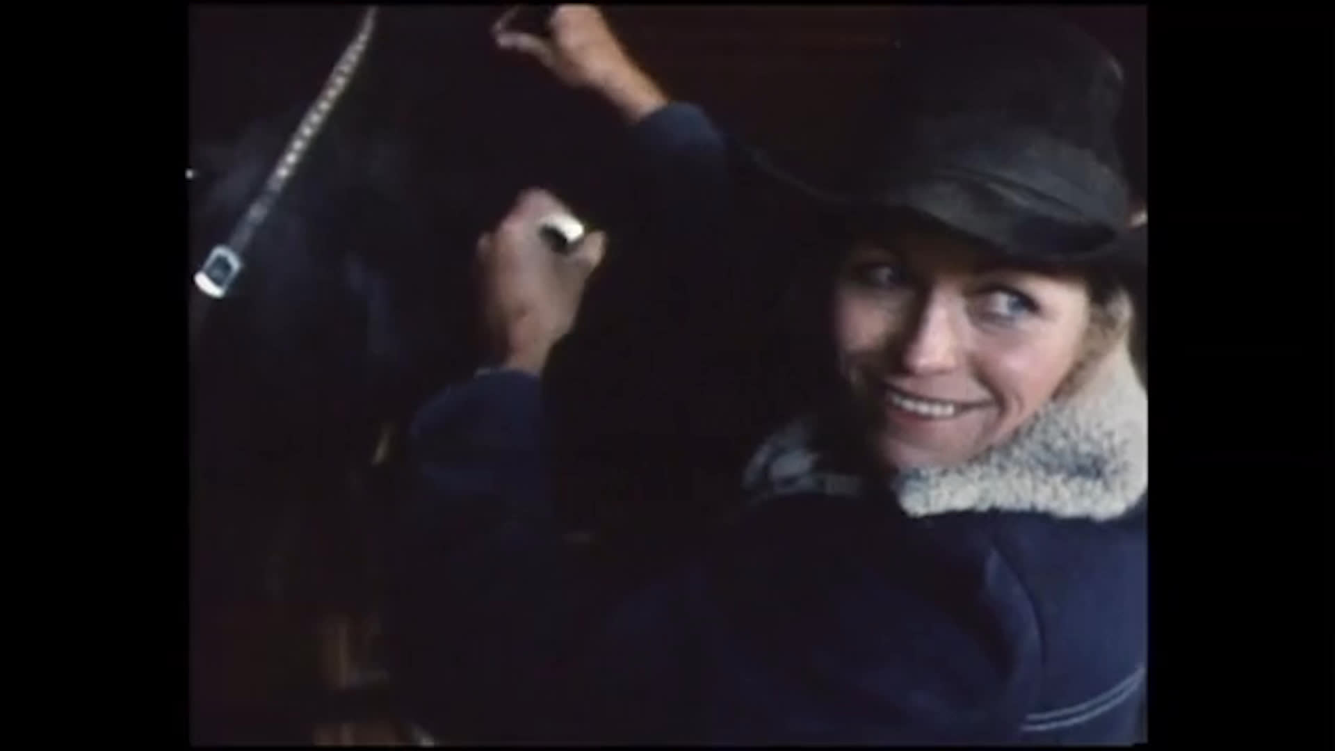 A woman adjusts horse tack in a dim stable, wearing a cowboy hat and a shearling-collar jacket. Archival ranch photographs accompany her account of growing up around horses with her grandfather and finding lasting comfort in ranch work.