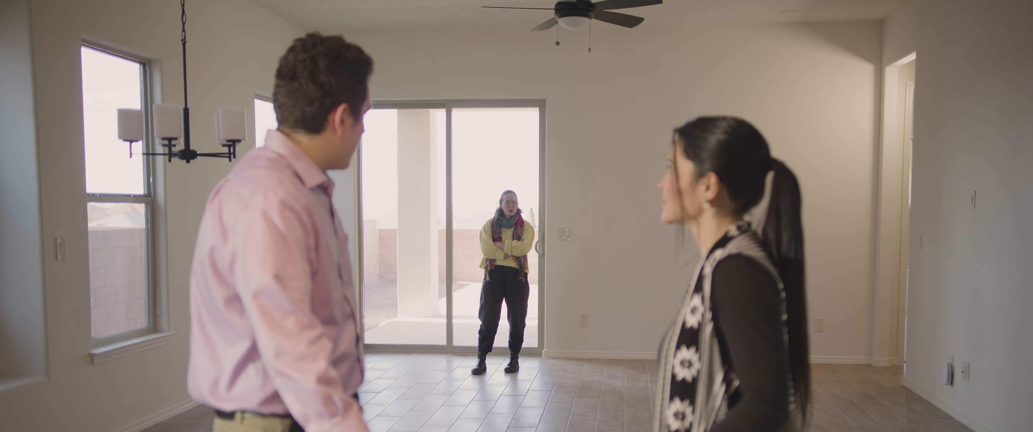 A man and a woman engage in a tense, animated argument within a spacious, minimalist living room while others observe in the background.