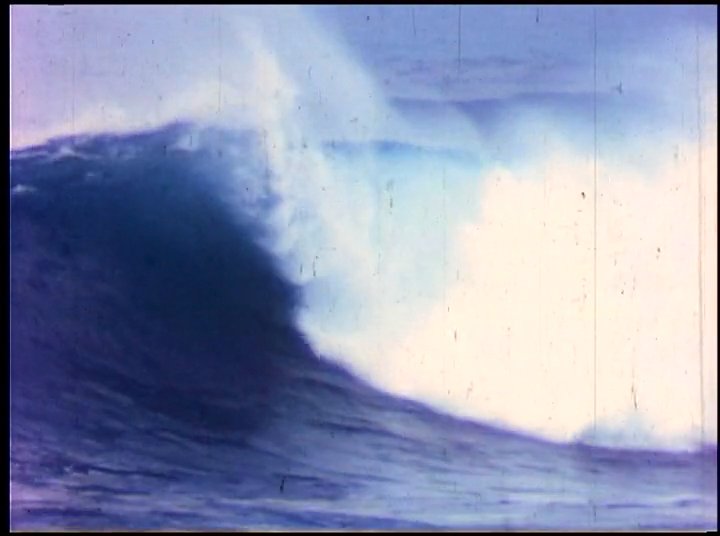 Vintage footage captures a surfer navigating a massive, crashing wave, interspersed with a contemporary interview of an individual reflecting on past surfing experiences.