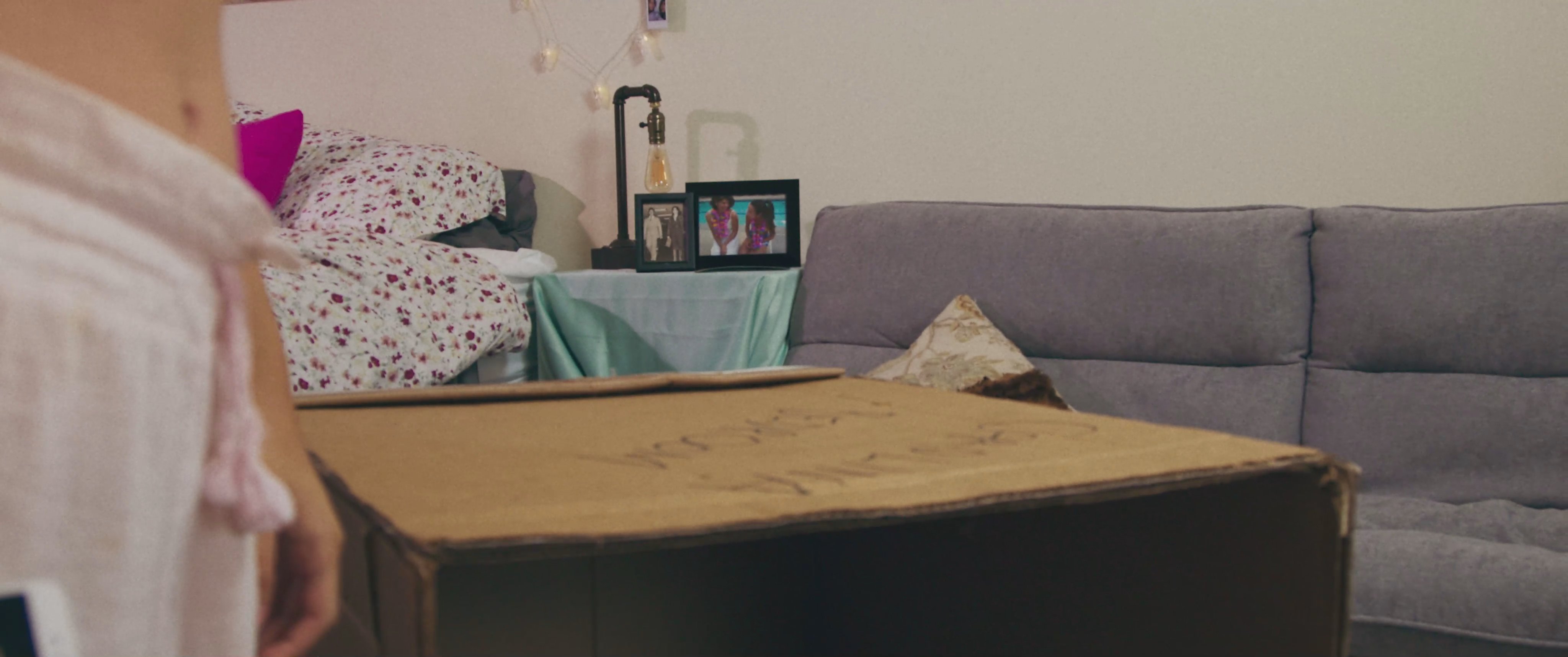 A young woman wakes up in her bedroom and begins exploring the contents of a large cardboard box, eventually retrieving and examining a collection of detailed sketches.