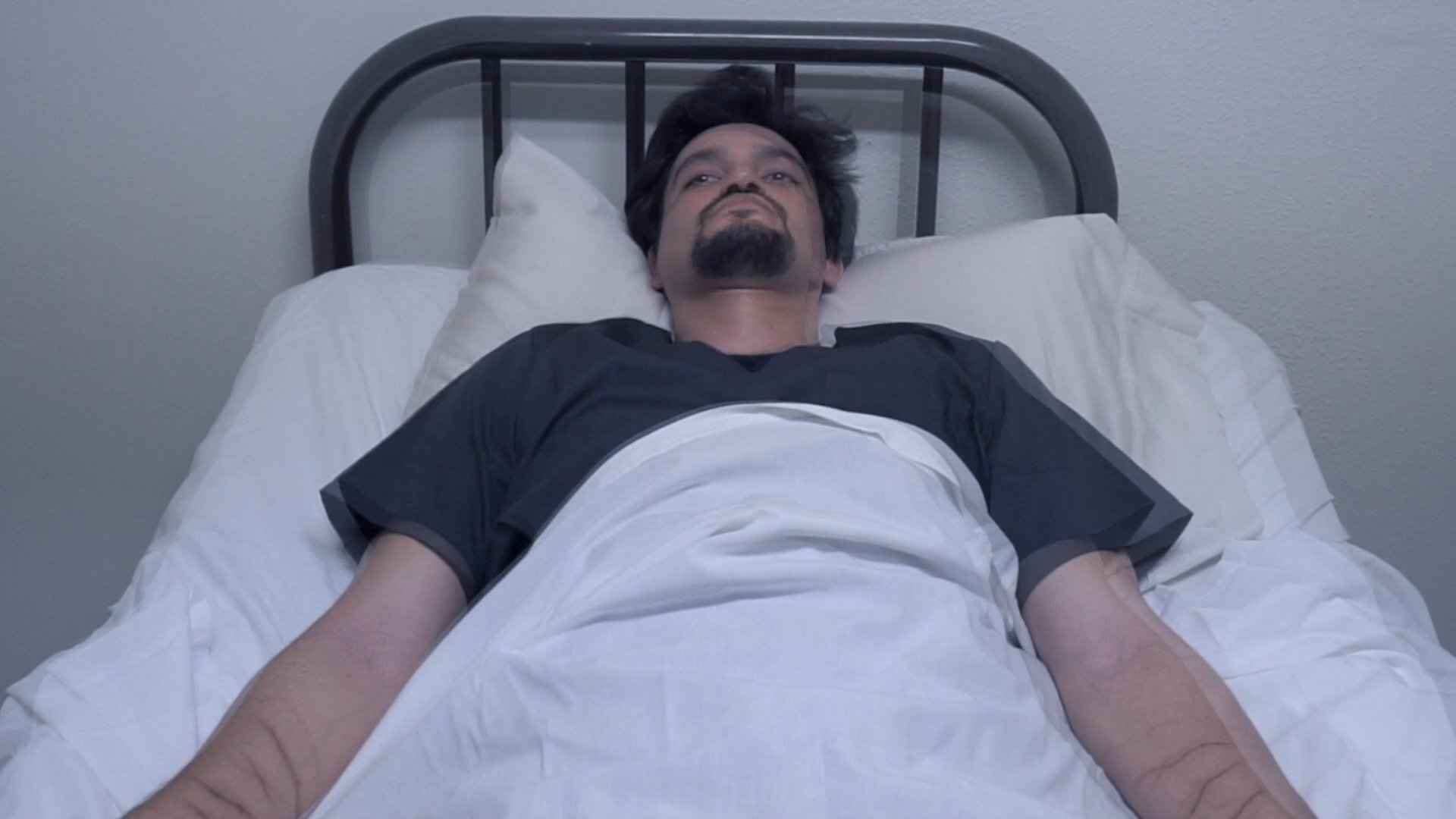 An older woman enters a room to attend to a man resting in a hospital bed. She provides care and comfort, ensuring he is settled during his recovery.