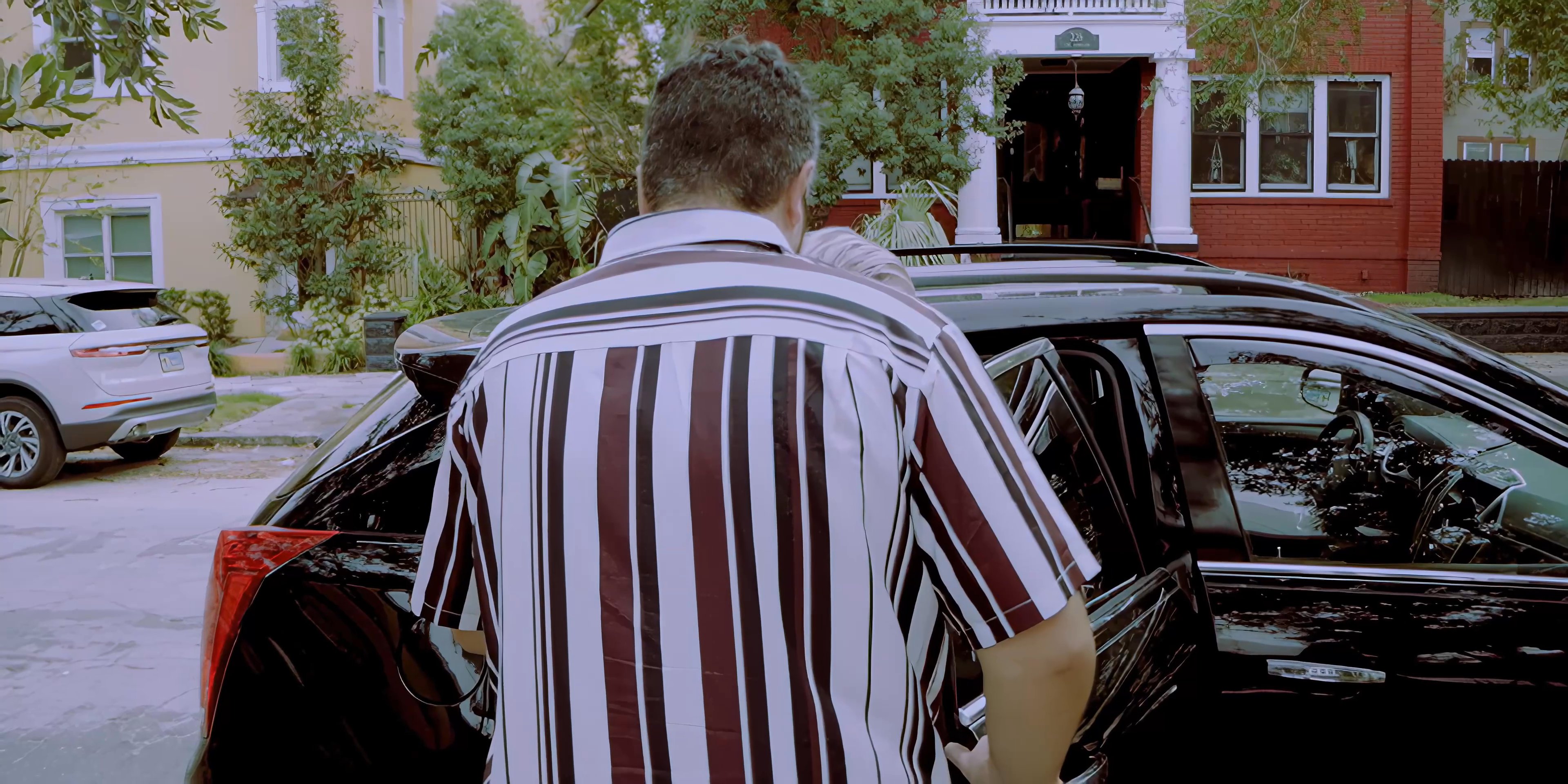 A man assists an elderly individual into the passenger seat of a black car before entering the vehicle to drive.
