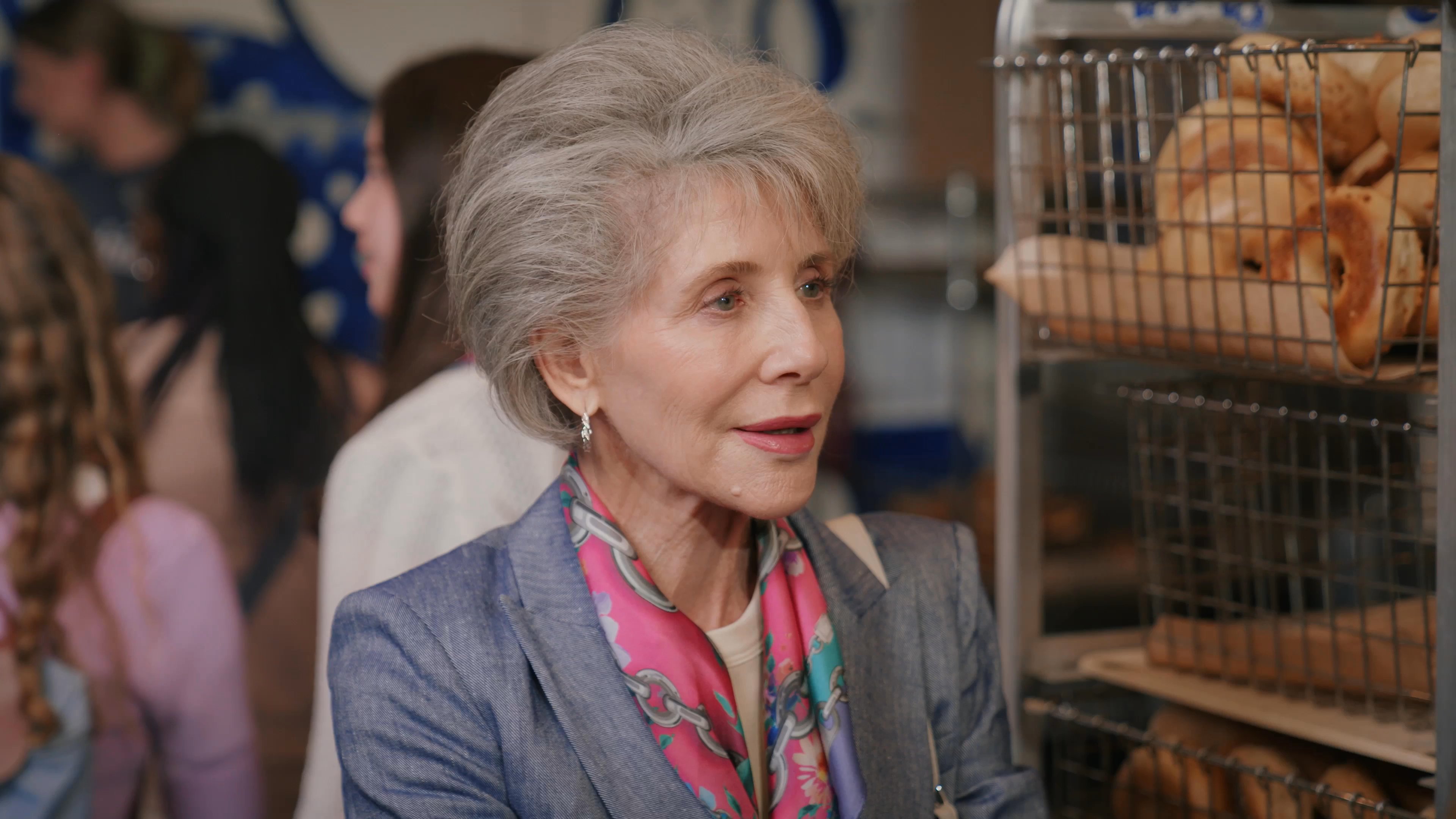 An older woman engages in an earnest conversation with a male bakery employee amidst shelves stocked with fresh breads.
