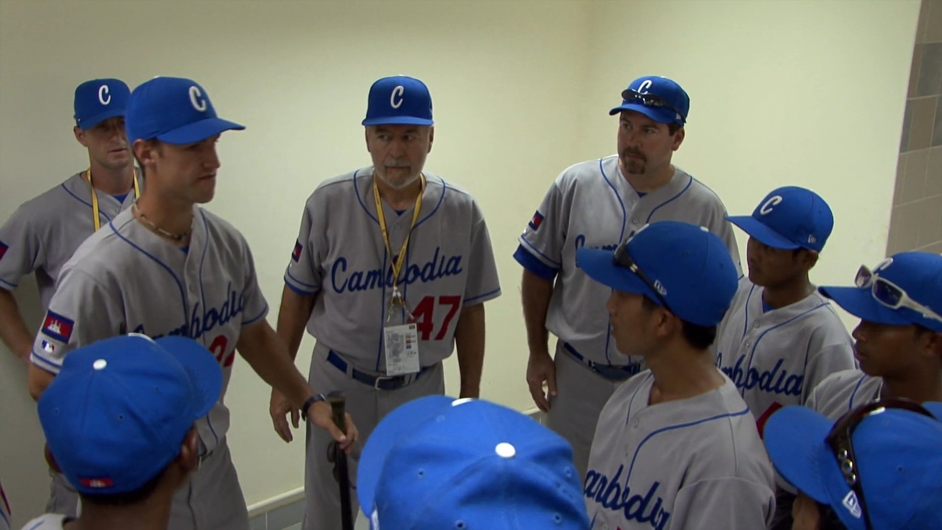 Members of the Cambodia national baseball team gather in an indoor huddle to receive instructions from their coaches before a game.