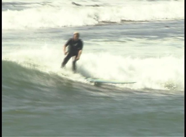 A surfer rides a wave in the ocean before an expert provides commentary on the performance in a studio setting.