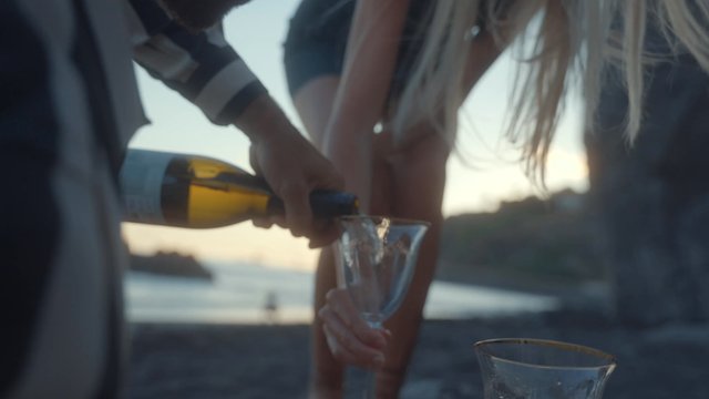A man pours champagne into a woman’s glass at the beach